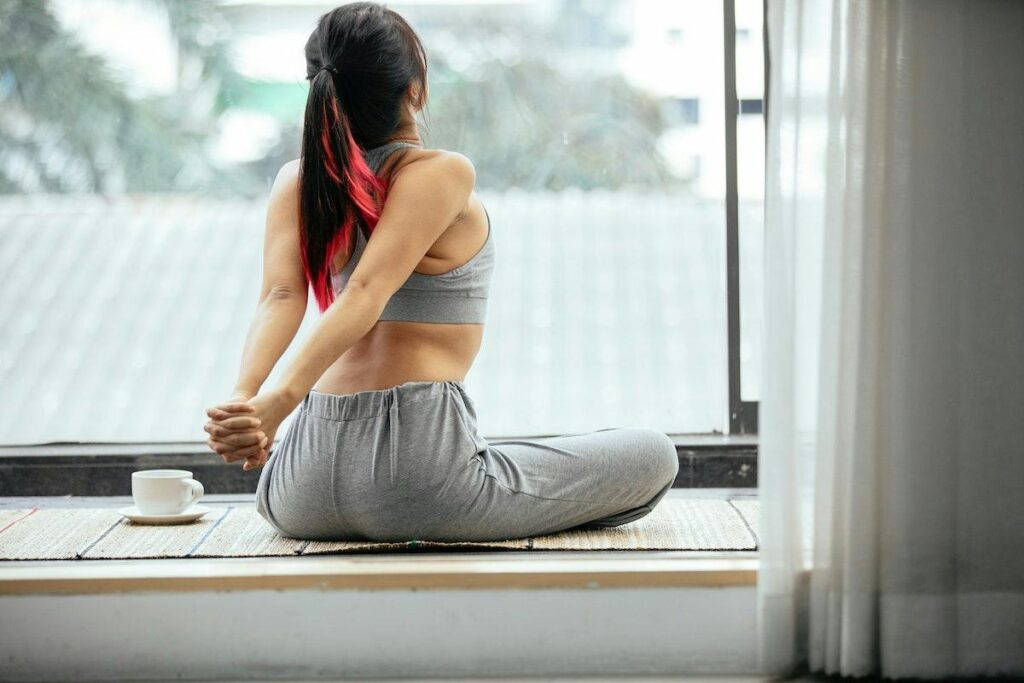 A woman is sitting on a window sill doing yoga.